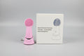 Pink multifunctional facial cleaning instrument with its packaging on a marble surface.